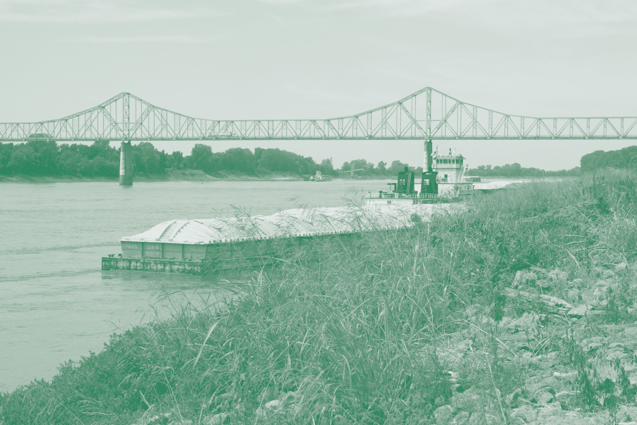 A green-tinted photograph of a towboat pushing a barge on the Mississippi River beneath a bridge